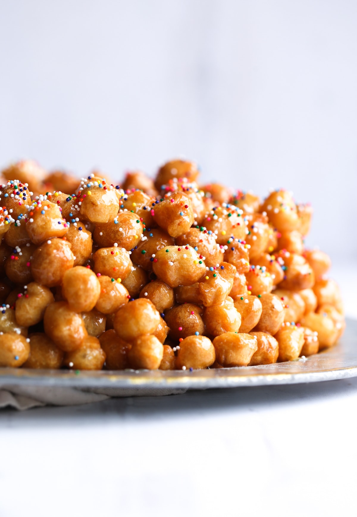 Struffoli piled on a serving platter topped with honey and sprinkles