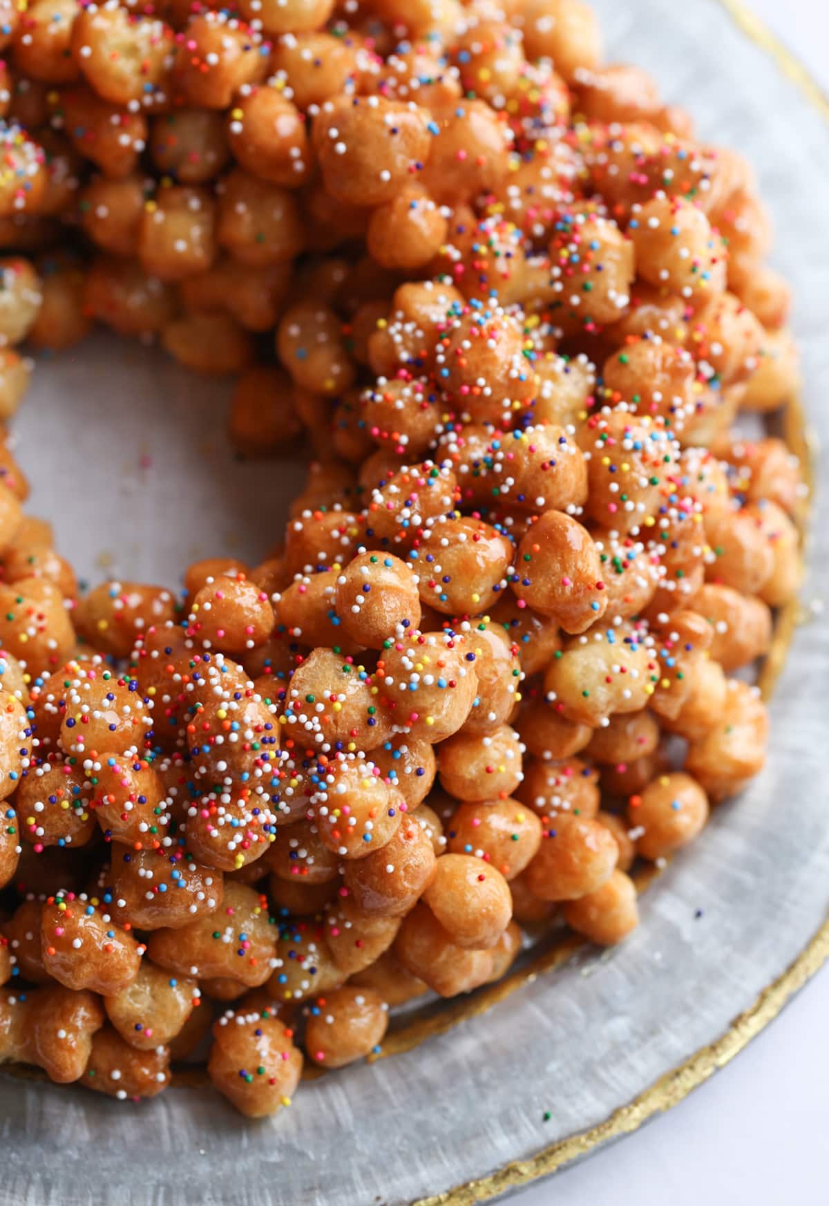 A pile of honey balls on a platter topped with nonpareil sprinkles