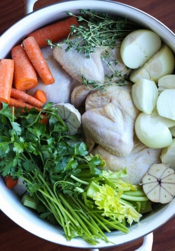 uncooked Chicken potatoes carrots and herbs in a pot