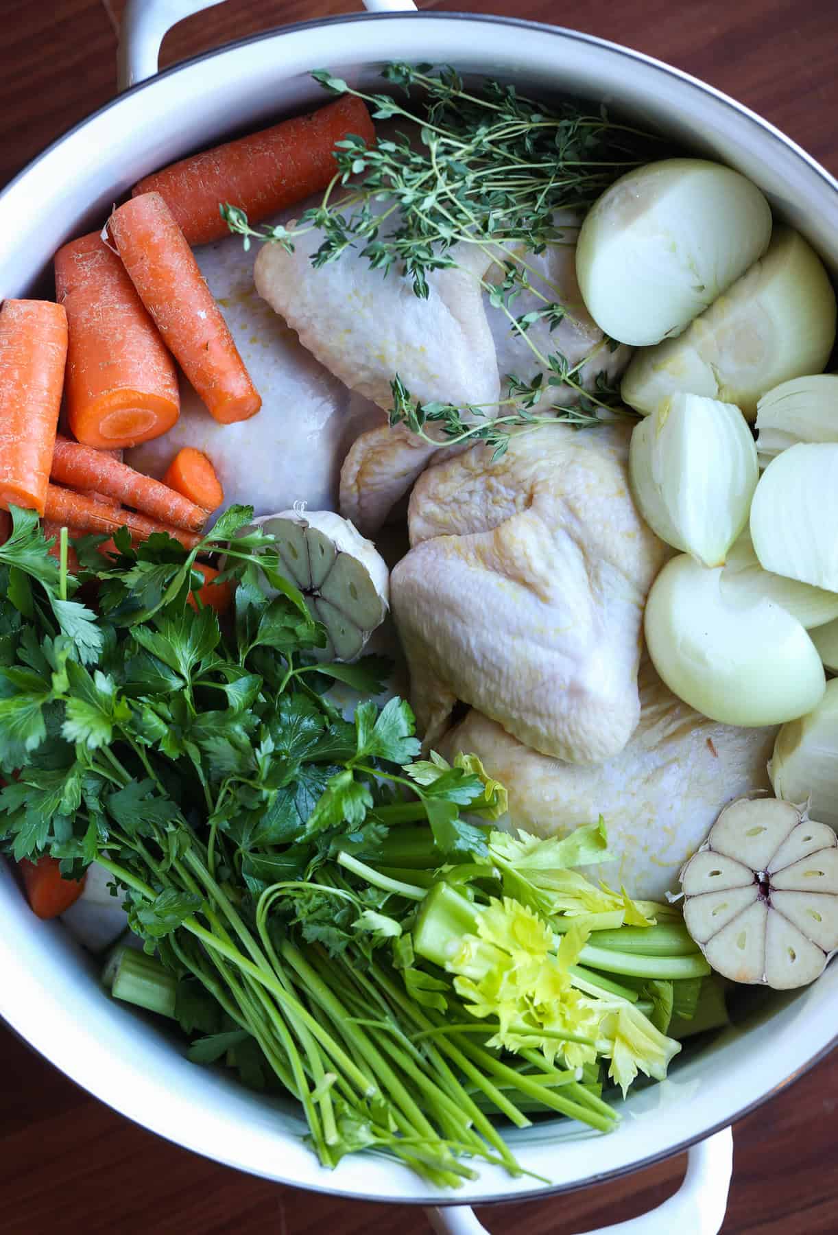 uncooked Chicken potatoes carrots and herbs in a pot