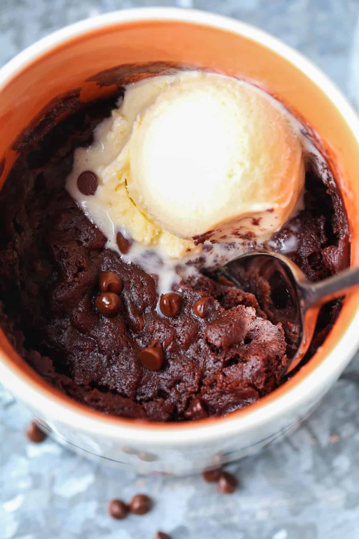 A close up of a brownie cooked in the microwave in a mug with a scoop of vanilla ice cream and a spoon