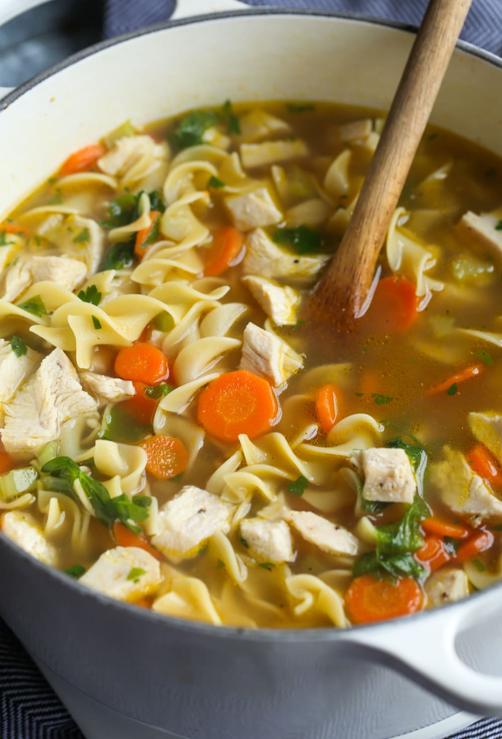 chicken noodle soup in a pot with a wooden spoon
