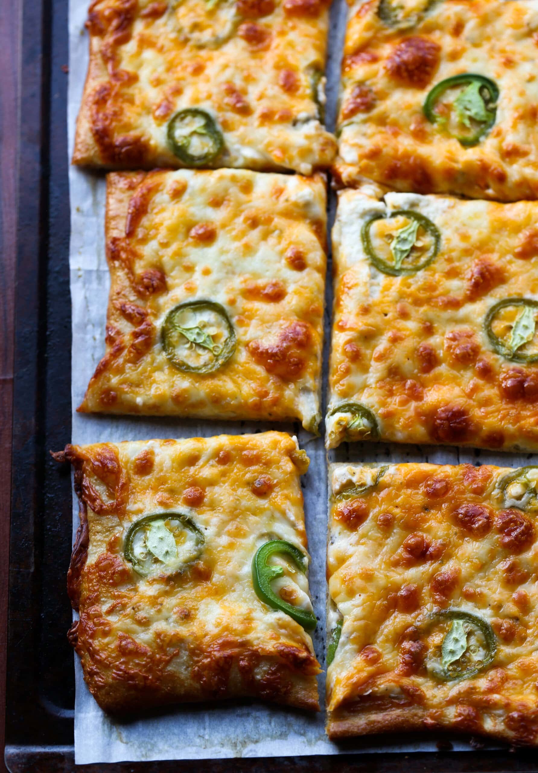 Pizza topped with jalapenos and cheese sliced on a tray