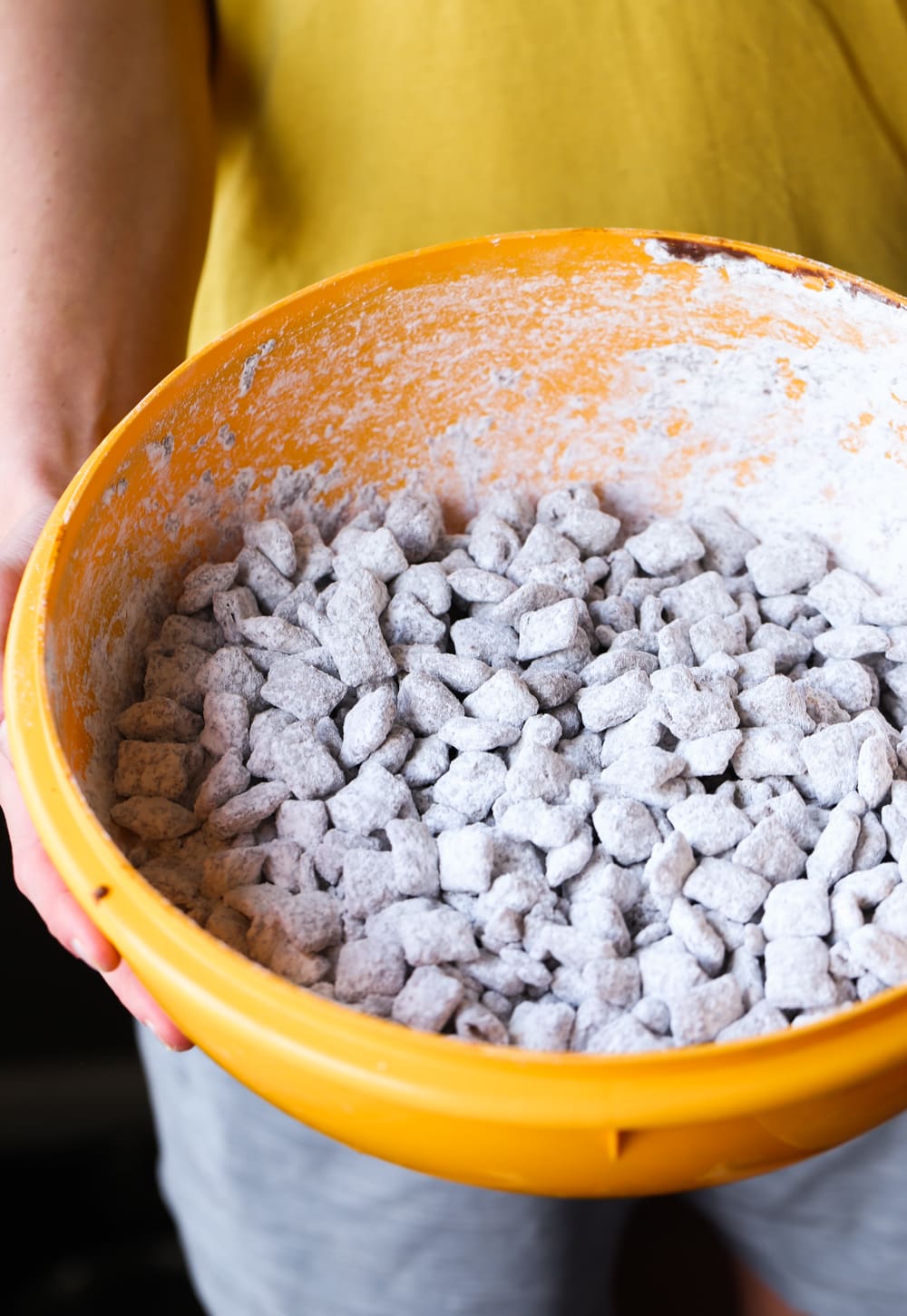 Shaking Puppy Chow with powdered sugar in a large bowl