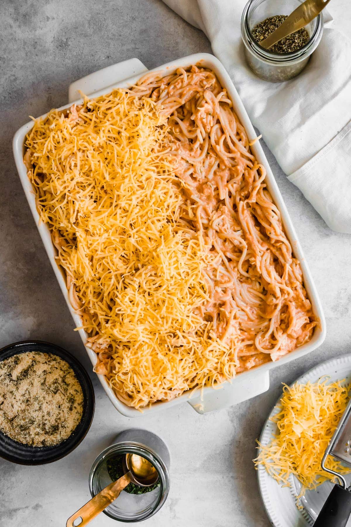 Spaghetti casserole with cheddar cheese being spread on top.