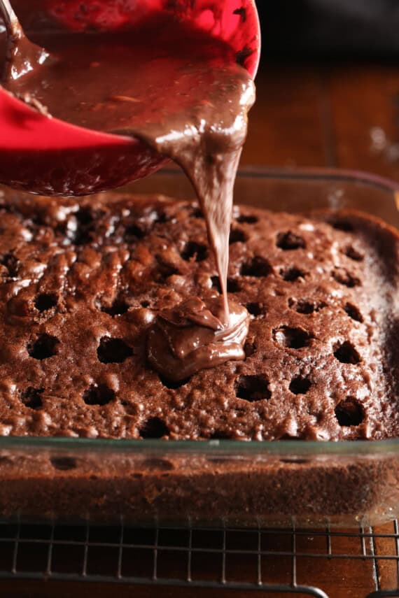 pouring chocolate ganache on top of a chocolate cake with holes pressed into the top