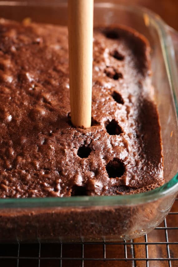 Poking holes in a baked chocolate cake with the back of a wooden spoon