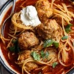 Bowl of spaghetti and meatball soup topped with parmesan cheese and ricotta