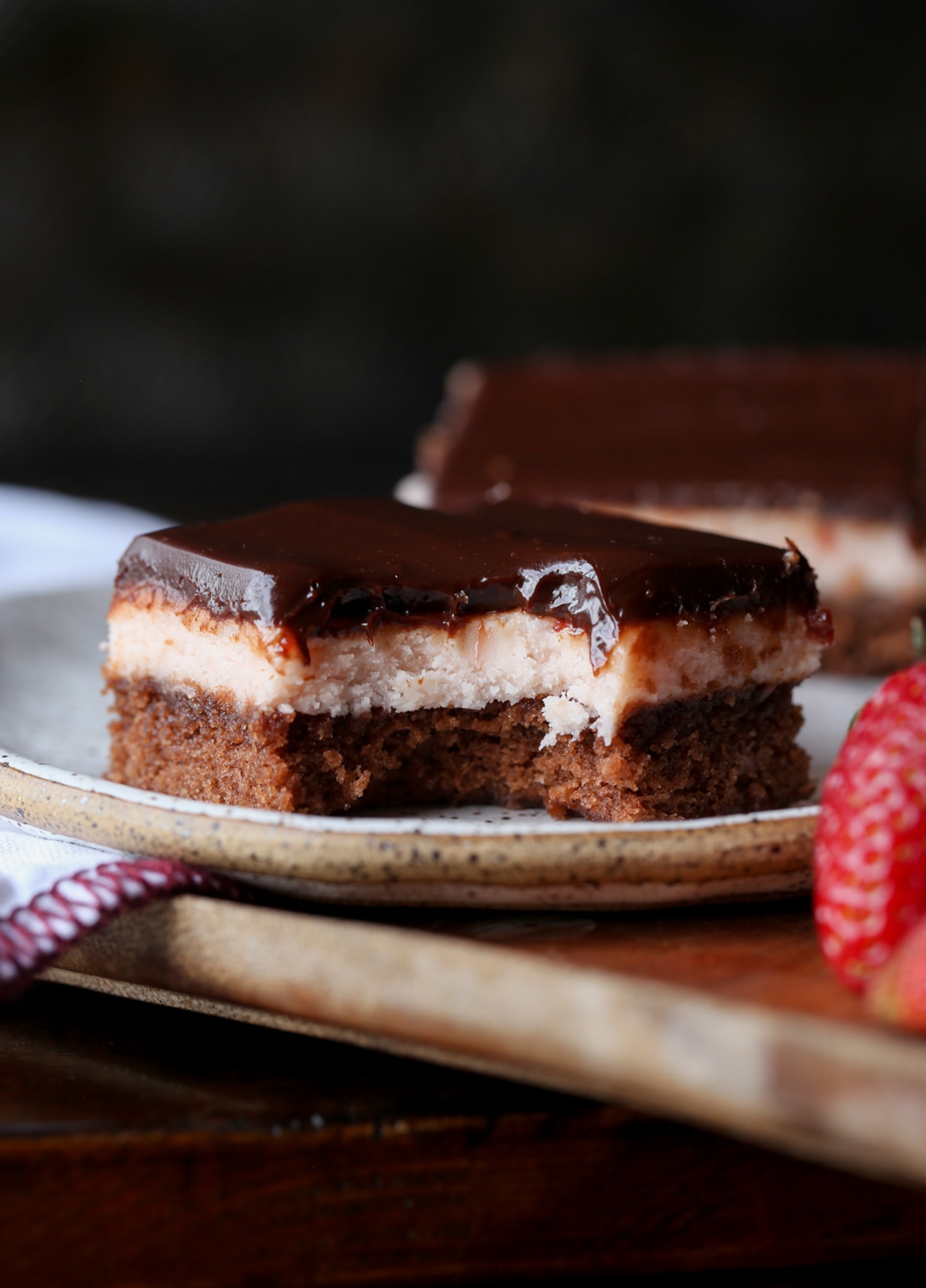 Ein Fudge-Brownie mit Erdbeer-Buttercreme und Schokoladen-Ganache, dazu ein Bissen auf einem Teller herausgenommen