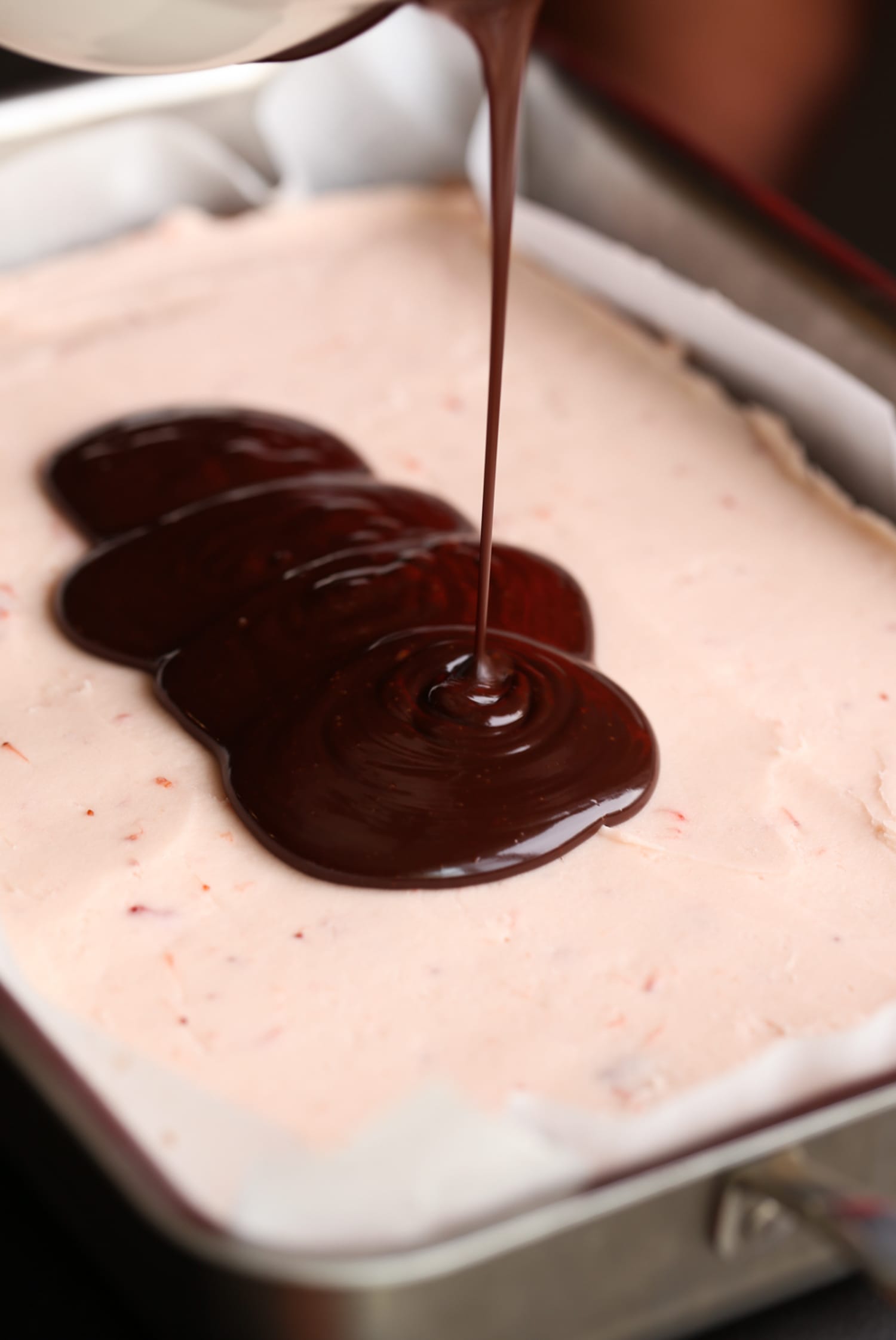 pouring chocolate ganache on top of strawberry buttercream in a 9x13 pan