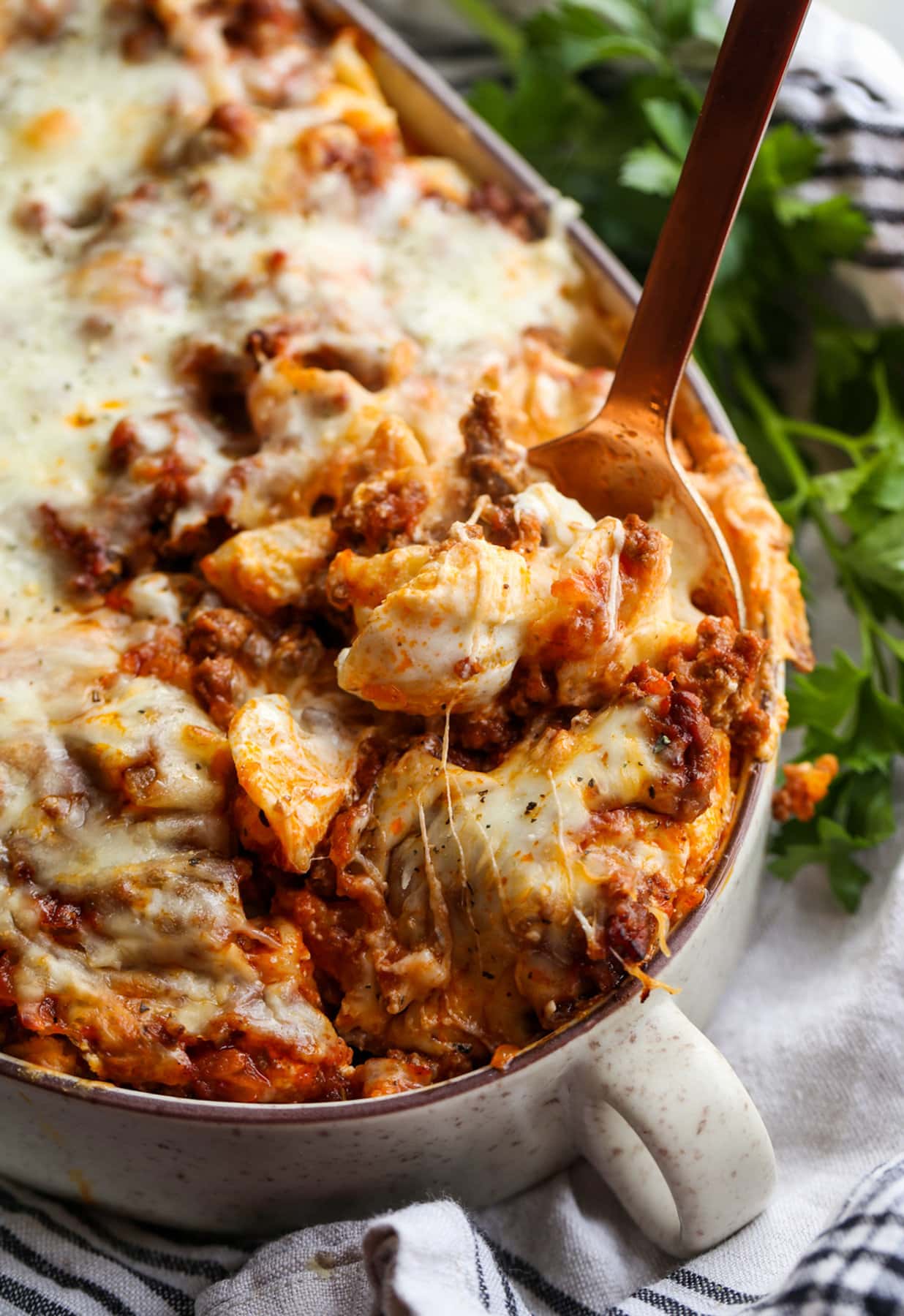 Unstuffed shells casserole with meat sauce, ricotta cheese, and marinara sauce topped with mozzarella being served with a spoon.