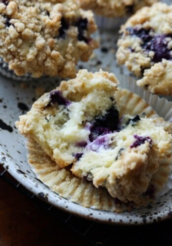 A blueberry muffin broken open to reveal the cream cheese filling, next to more muffins on a plate.