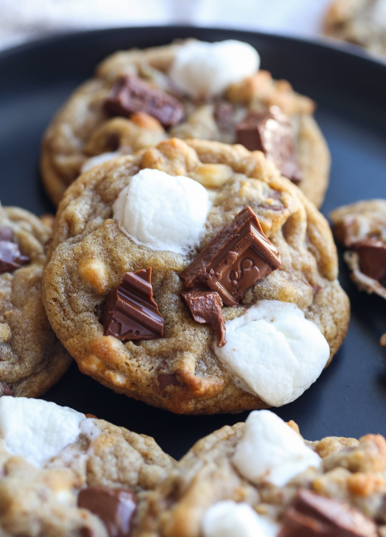 Close up of s'mores cookies on a wire rack topped with melted milk chocolate and mini marshmallows