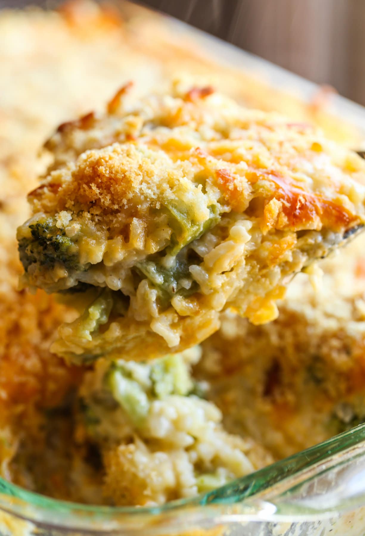 Scooping out a portion of broccoli rice bake with cheese in a casserole dish.