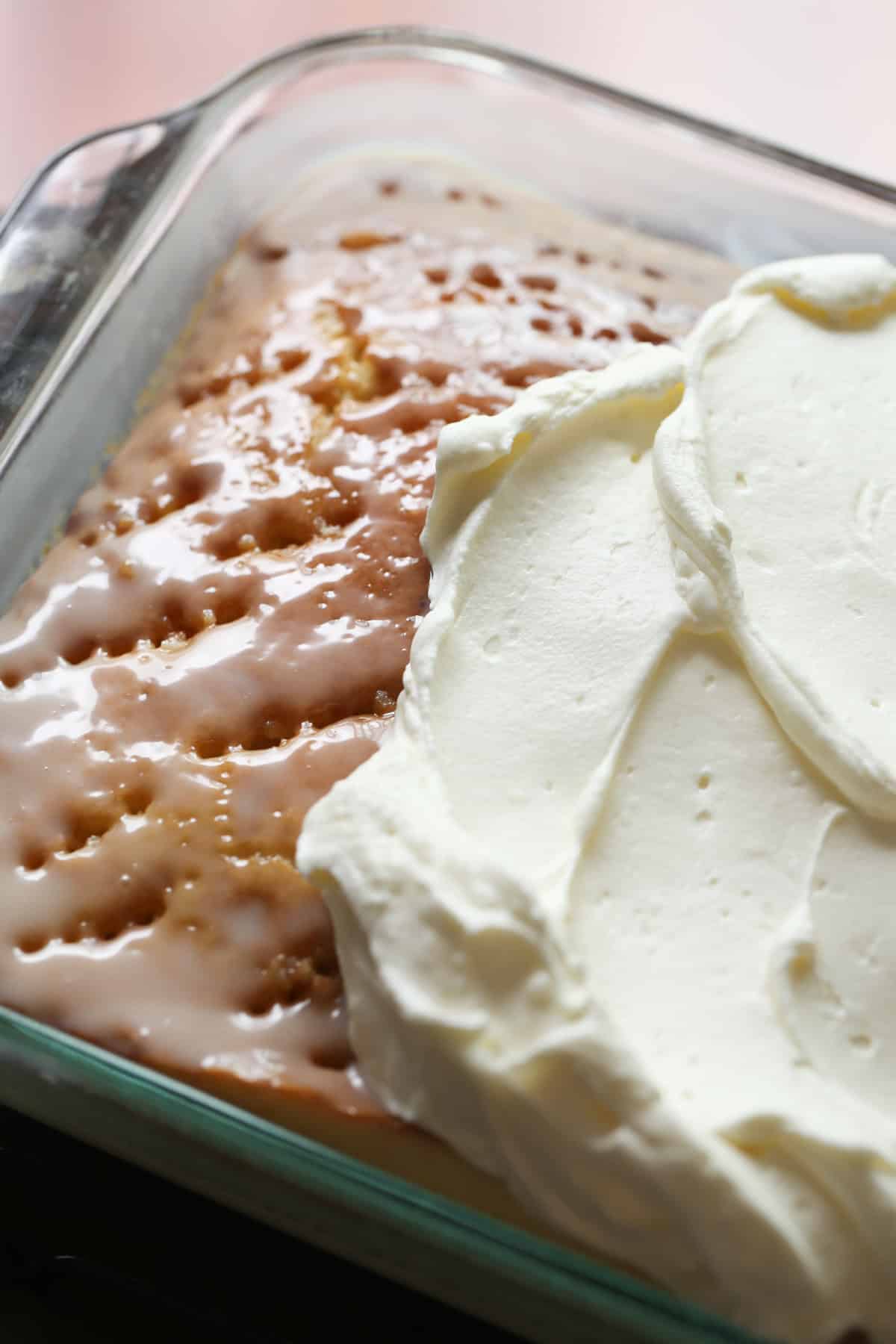 Poke cake being frosted with whipped topping
