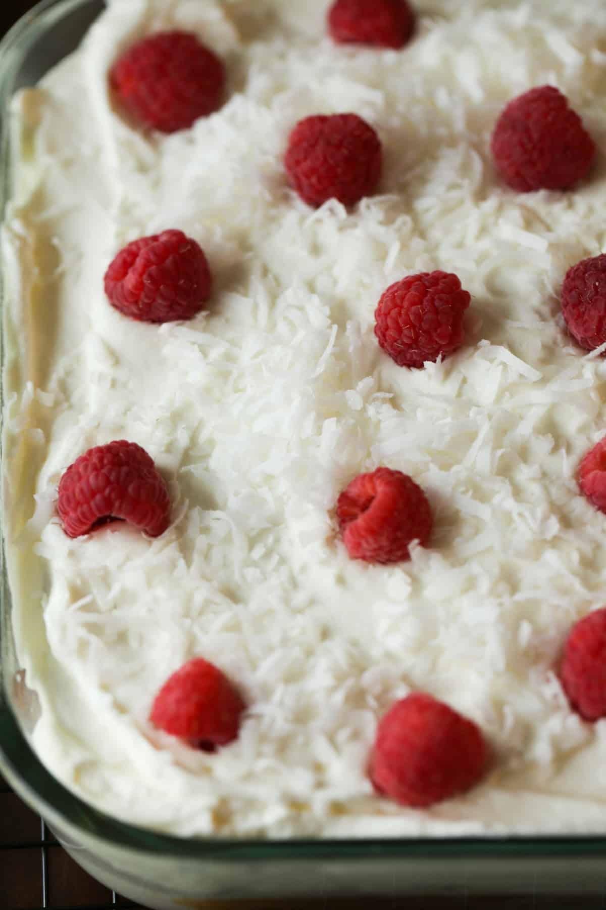 Coconut Cake in a 9x13 pan topped with coconut frosting, sweetened flaked coconut, and raspberries.