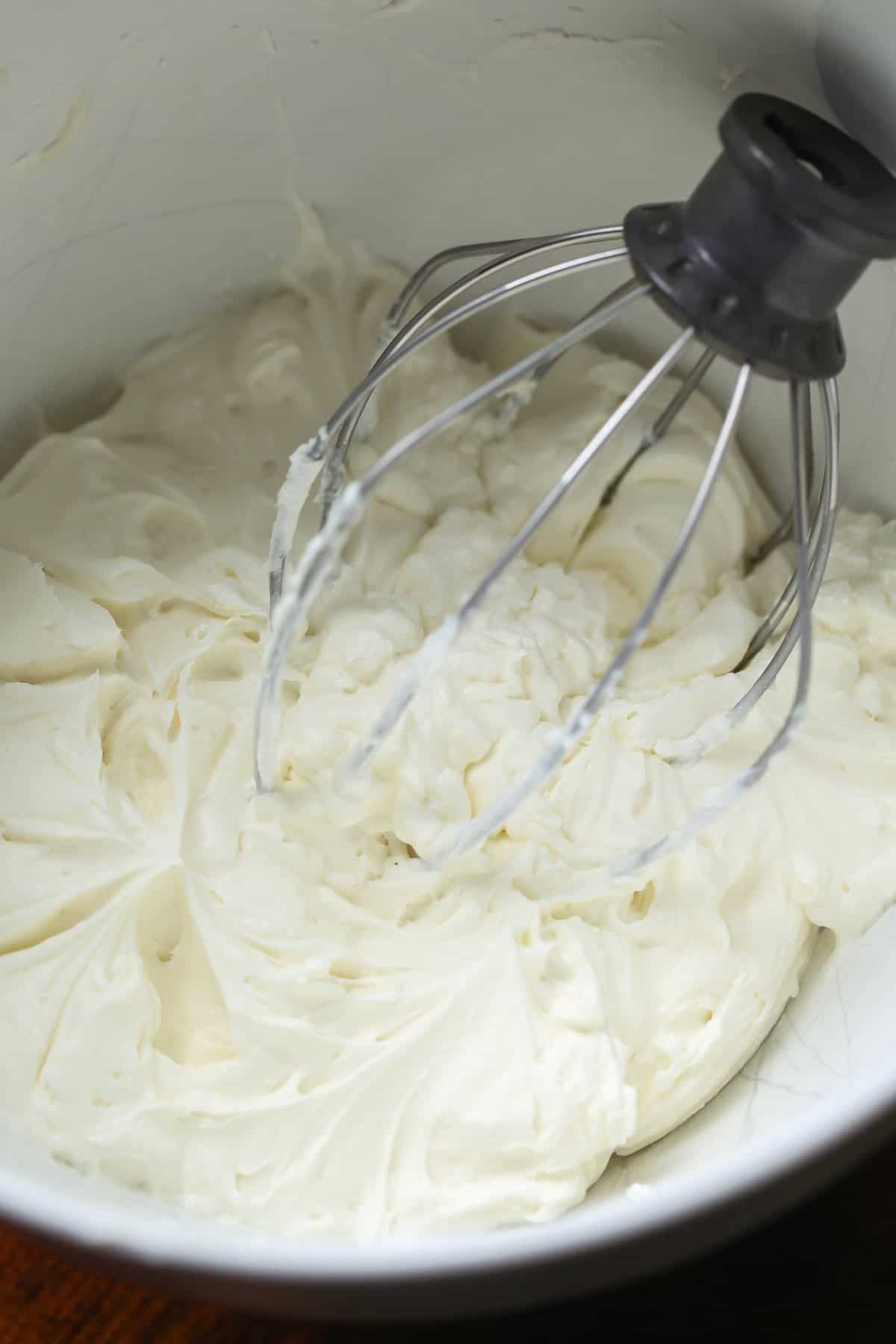 Fluffy Whipped Frosting in a silver mixing bowl with the whisk attachment in the frosting.