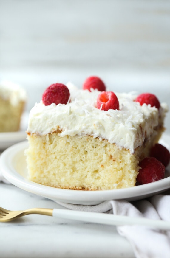 Slice of Coconut Poke Cake on a plate topped with whipped frosting