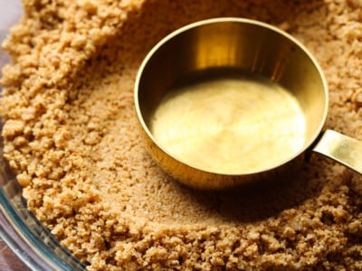 Measuring cup pressing into a graham cracker crust.
