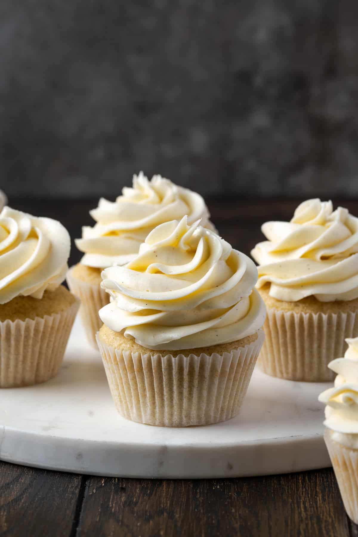 Cupcakes frosted with swirls of Swiss meringue buttercream frosting on a marble cake stand.