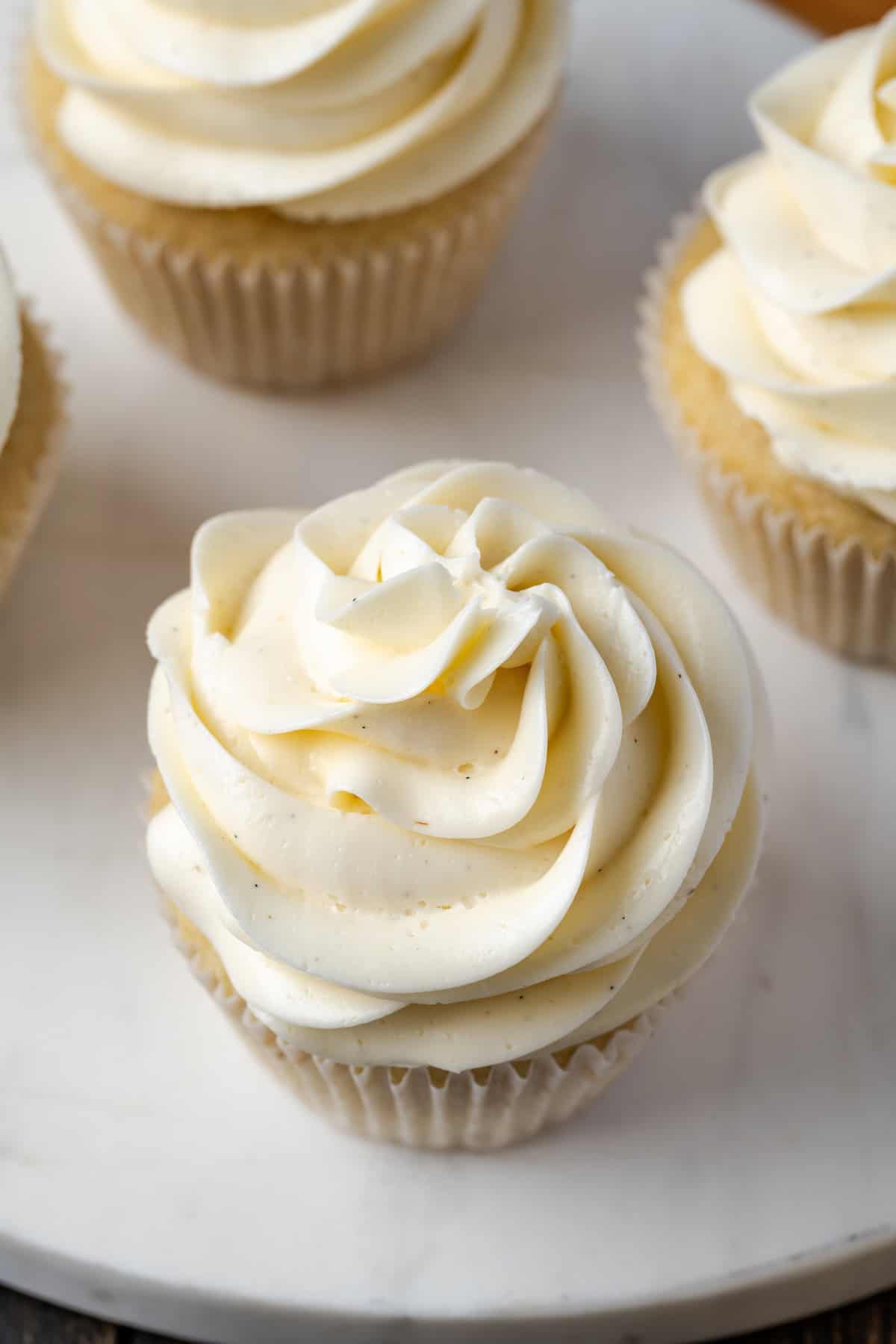 Close up of cupcakes frosted with swirls of Swiss meringue buttercream frosting on a marble cake stand.