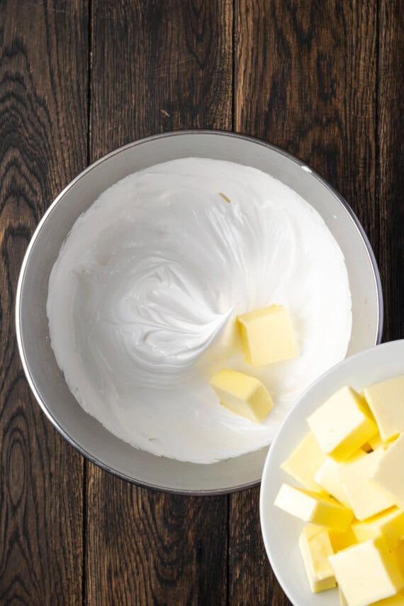 Cubes of butter being added to a bowl of whipped egg whites.