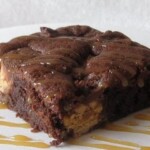 A Fudgy Cake Mix Snickers Brownie on a White Plate Drizzled with Caramel Sauce