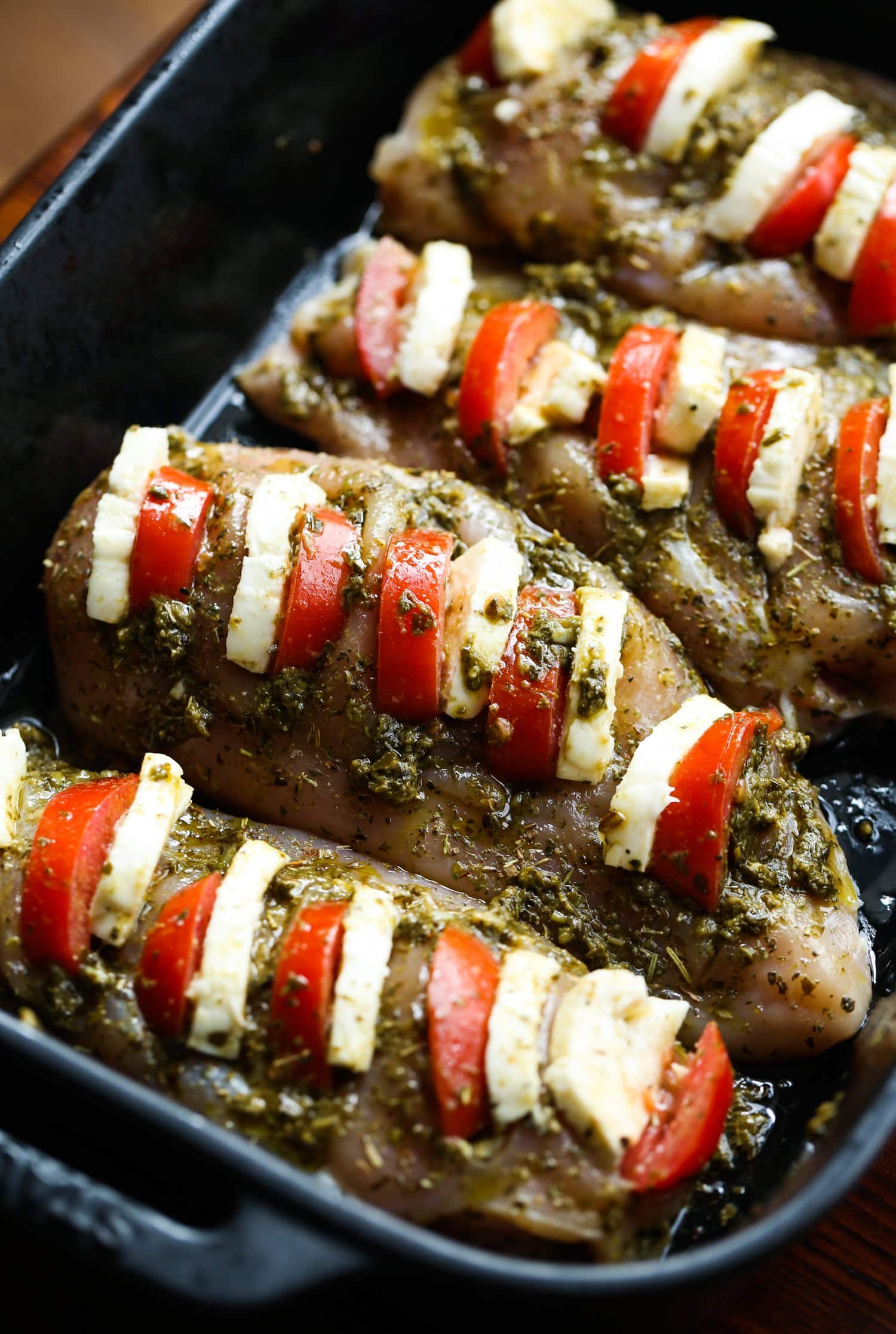 raw chicken breasts stuffed with tomato, mozzarella , and pesto in a baking dish