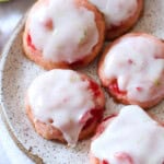 Pink cherry cookies with lime icing drizzled on top on a stoneware plate