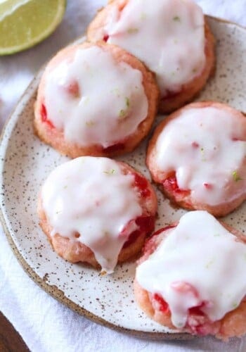 Pink cherry cookies with lime icing drizzled on top on a stoneware plate