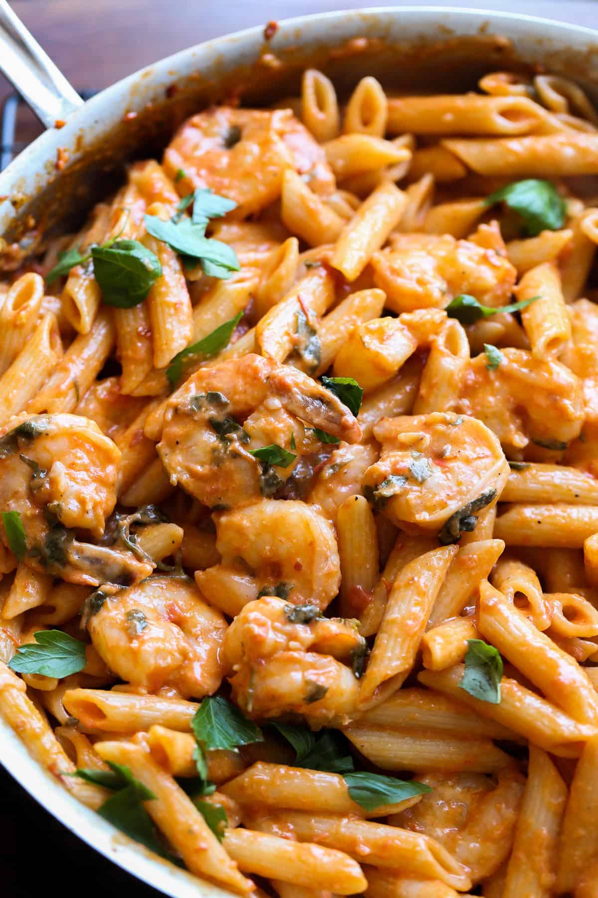A stainless skillet with shrimp pasta in a creamy tomato sauce.