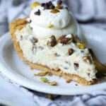 cannoli pie sliced on a plate topped with pistachios and chocolate chips