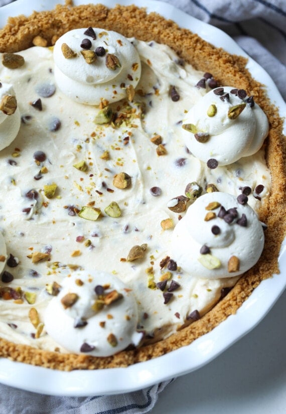 Cannoli pie in a pie dish topped with whipped cream and pistachios