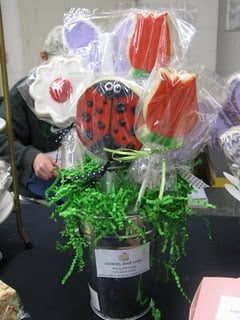 A Container of Spring-Themed Sugar Cookies Attached to Sticks and Wrapped in Plastic Wrap