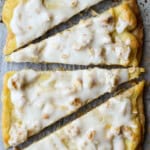 Danish Kringle topped with nuts and icing cut into triangular slices on a parchment lined baking sheet