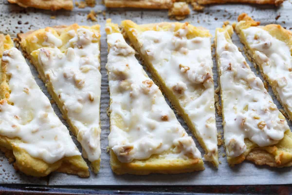 Danish Krisgle cut into slices topped with walnuts and icing on a parchment lined baking sheet