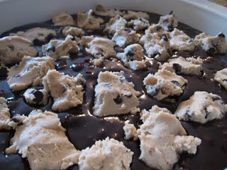 Brownie batter in a pan with chunks of raw chocolate chip cookie dough on top