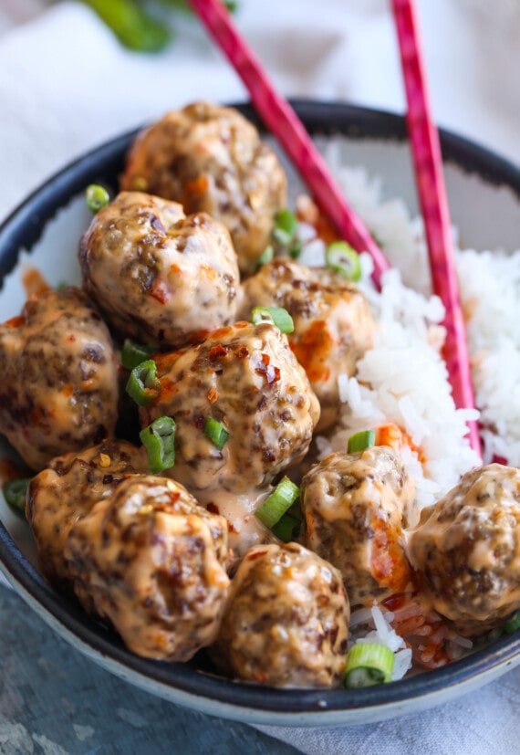 A bowl of bang bang meatballs with chopsticks and rice.
