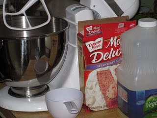 A box of strawberry cake mix beside a mixing bowl fitted with the whisk attachment