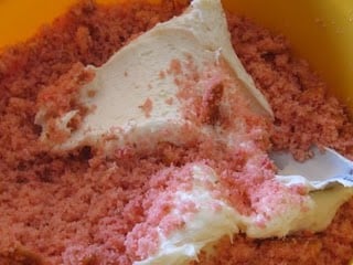 Cream cheese icing and crumbled strawberry cake inside of a large bowl