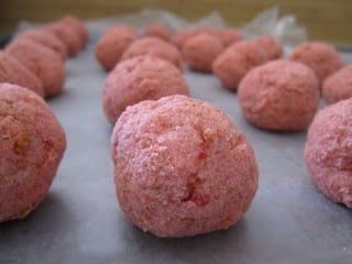 Balls of the cream cheese and strawberry cake crumb mixture on a baking sheet