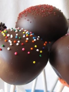Three strawberry cake pops covered in chocolate and topped with sprinkles