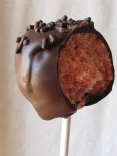 A strawberry cake mix cupcake pop on a stick with a bite taken out of it
