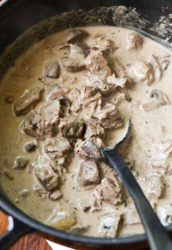 A creamy beef stroganoff sauce being stirred with a spoon.