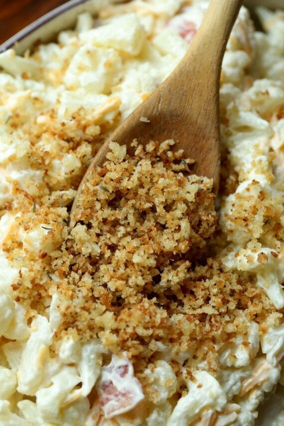 Unbaked cauliflower casserole being topped with toasted breadcrumbs.