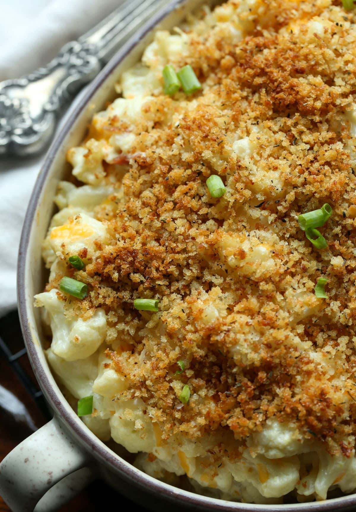 A shot of a baked cauliflower casserole topped with breadcrumbs and garnished with green onion.