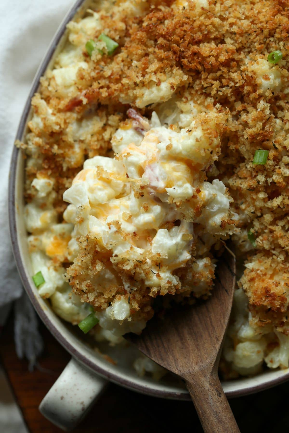 A wooden serving spoon digging into a cauliflower casserole.