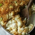 A cheesy cauliflower casserole with portions scooped out, and a wooden spoon resting in the dish.
