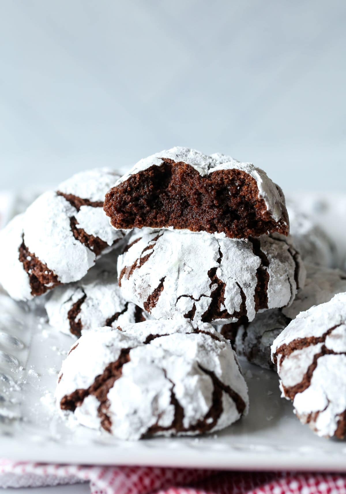 Several crinkle cookies on a clear glass plate. The cookie on top of the pile has been broken apart to show the crumb.