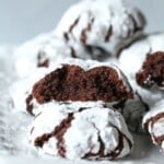 Chocolate crinkle cookies on a white plate, with one of the cookies broken in half and the broken sides facing the camera.
